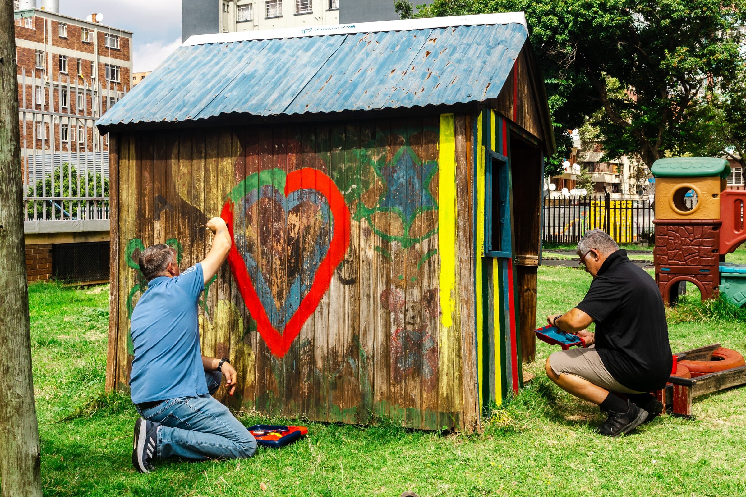 Volunteers painting a red heart onto a yellow wooden structure at Dinaledi Crèche