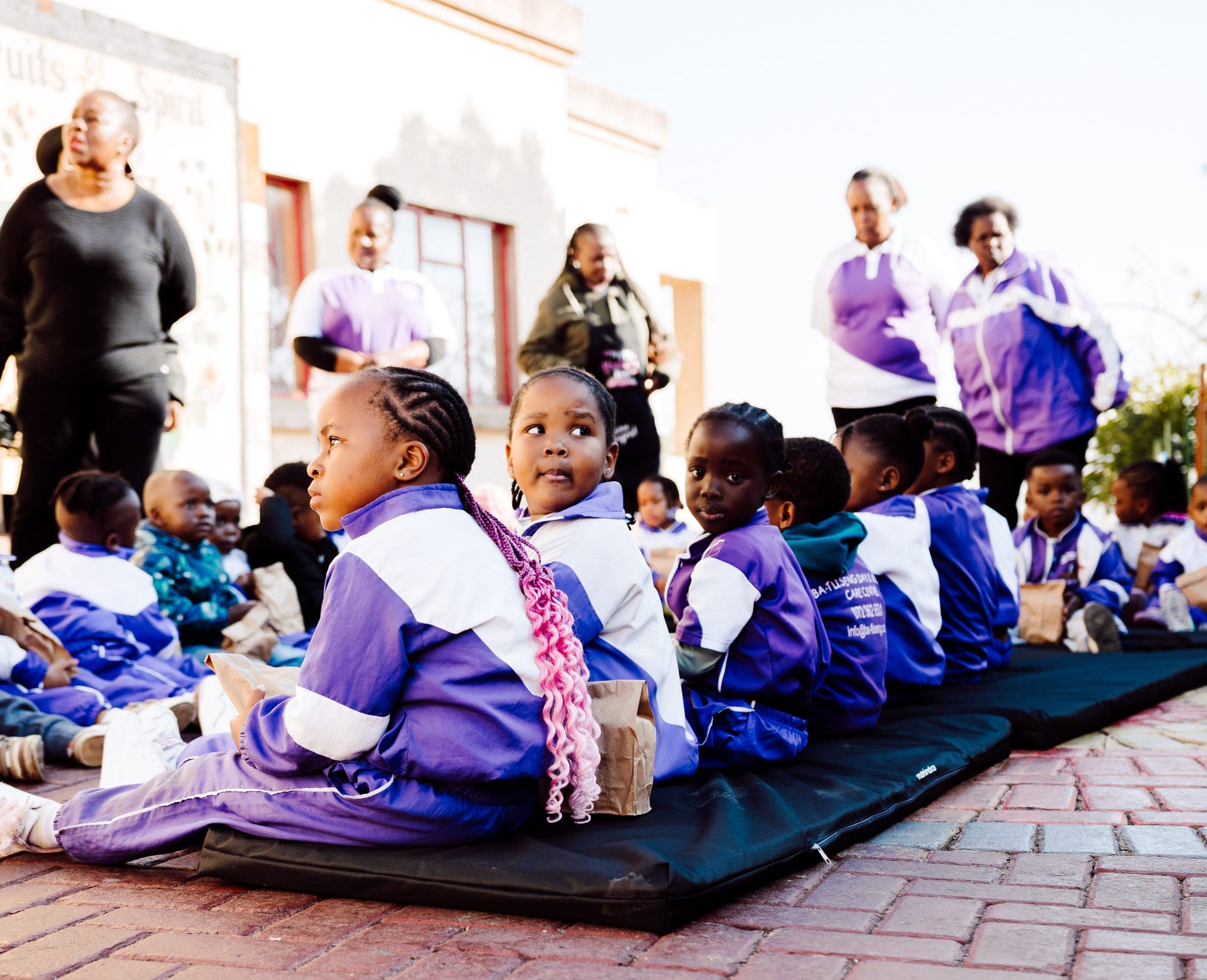 Children seated on new black mats holding food parcels at Ba-Tliseng