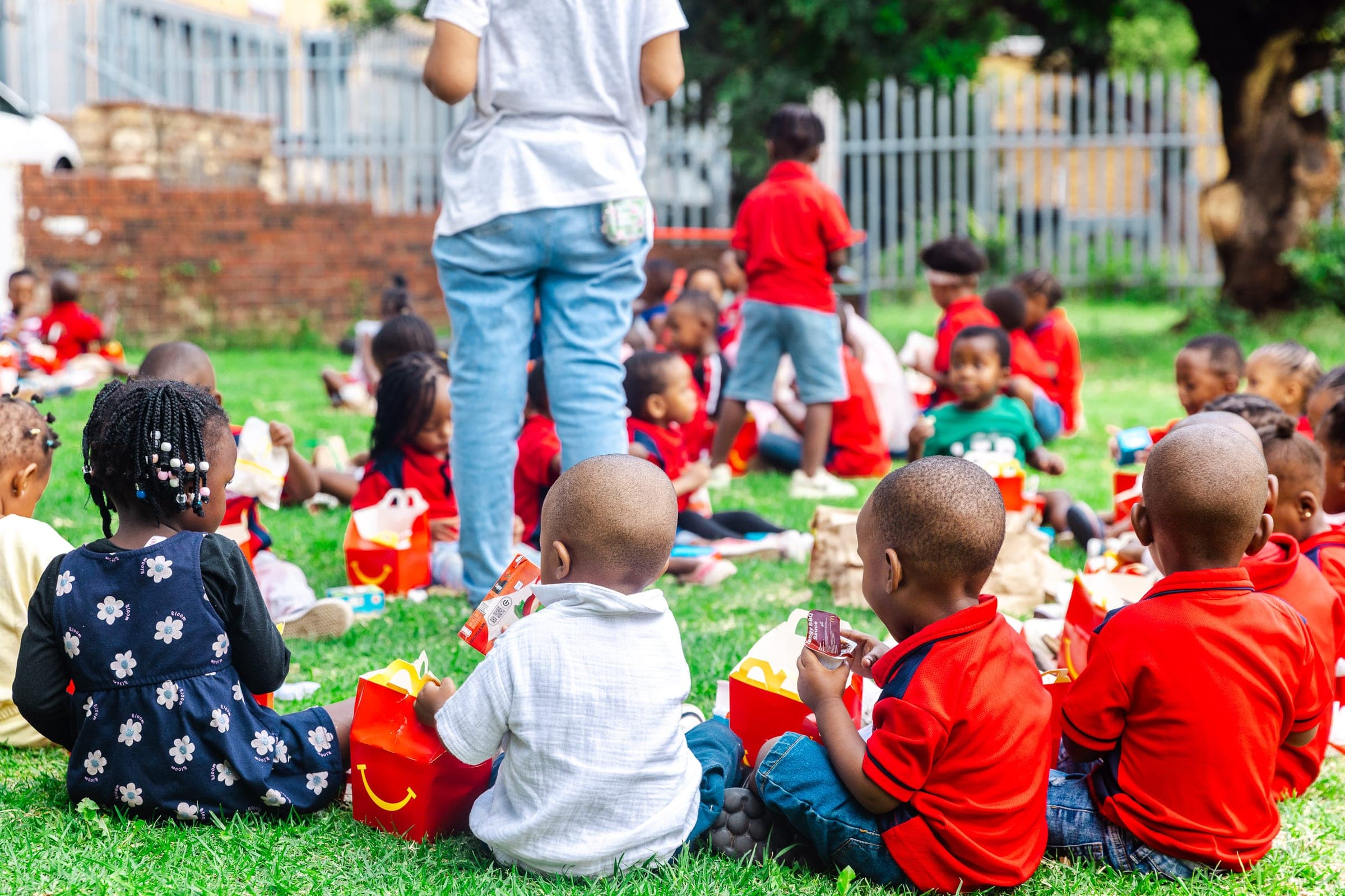 Children sitting together on the grass at Dinaledi Crèche