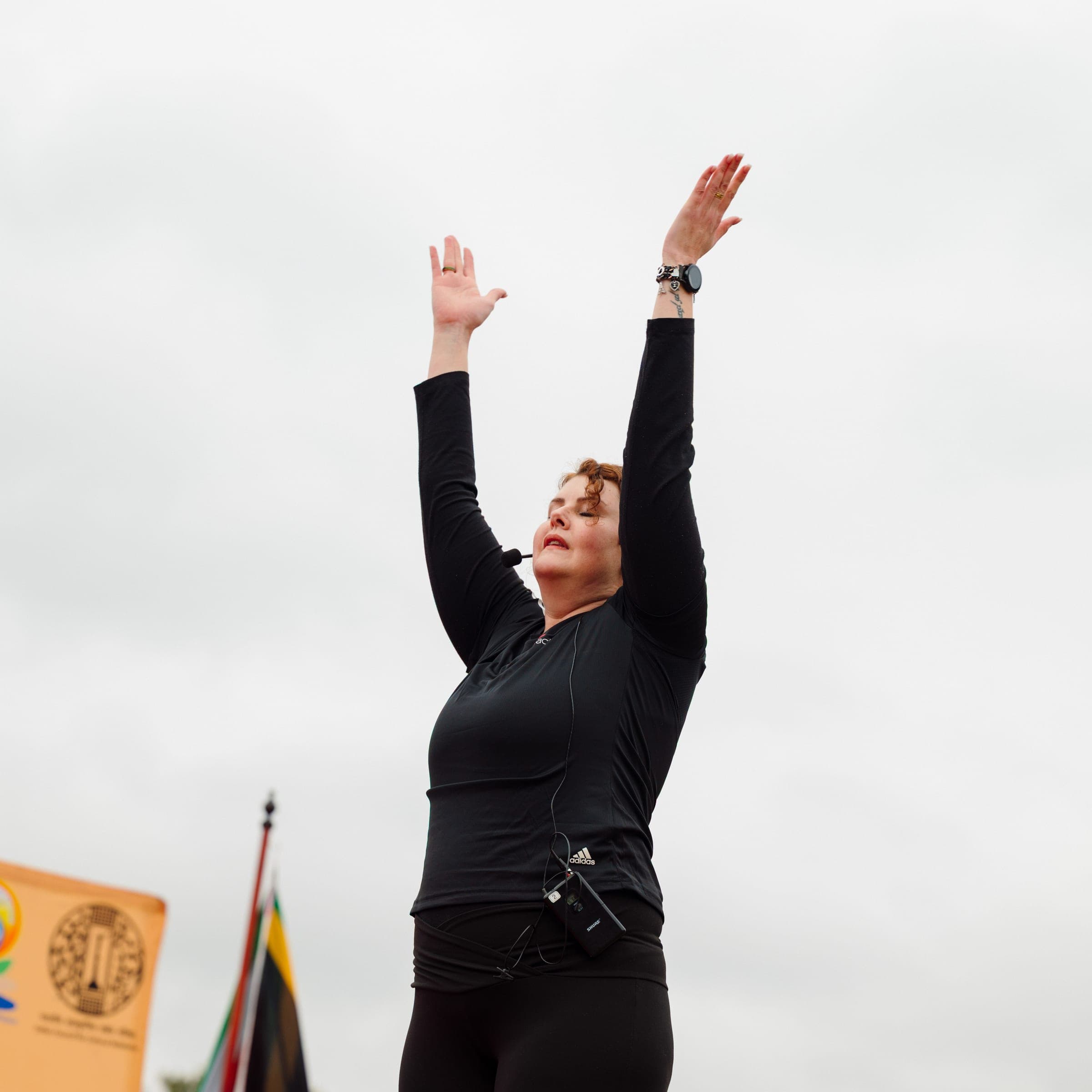 Yoga instructor with arms raised leading a stretch outdoors