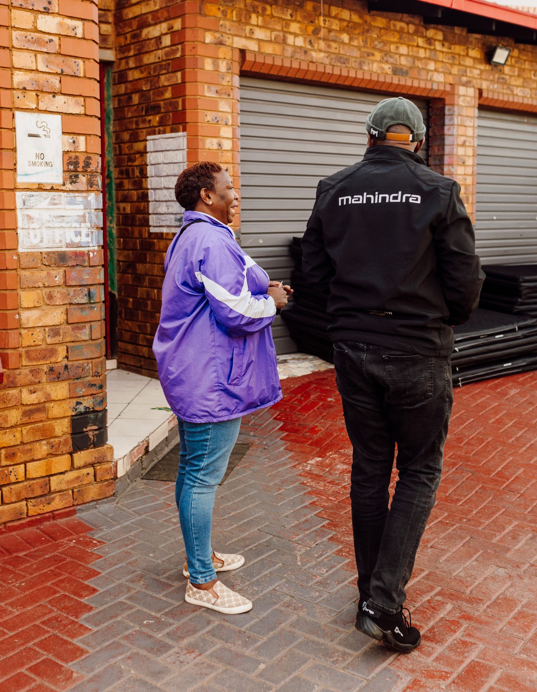 A Ba-Tliseng caregiver smiling with a Mahindra team member beside stacked mats