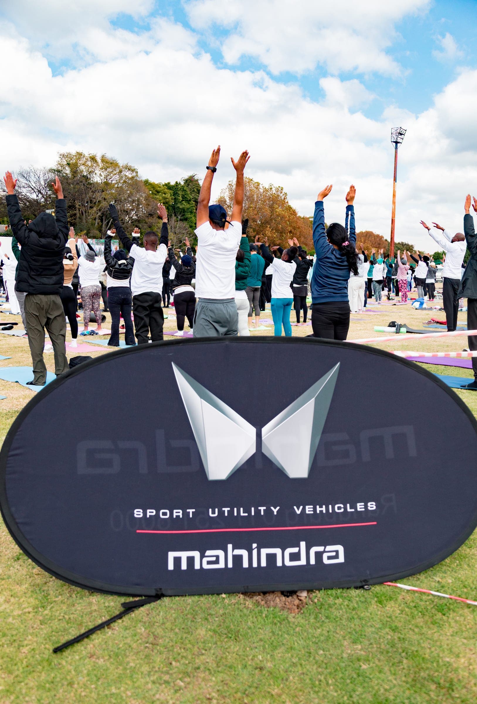 Yoga participants on mats near a Mahindra Sports Utility Vehicles banner