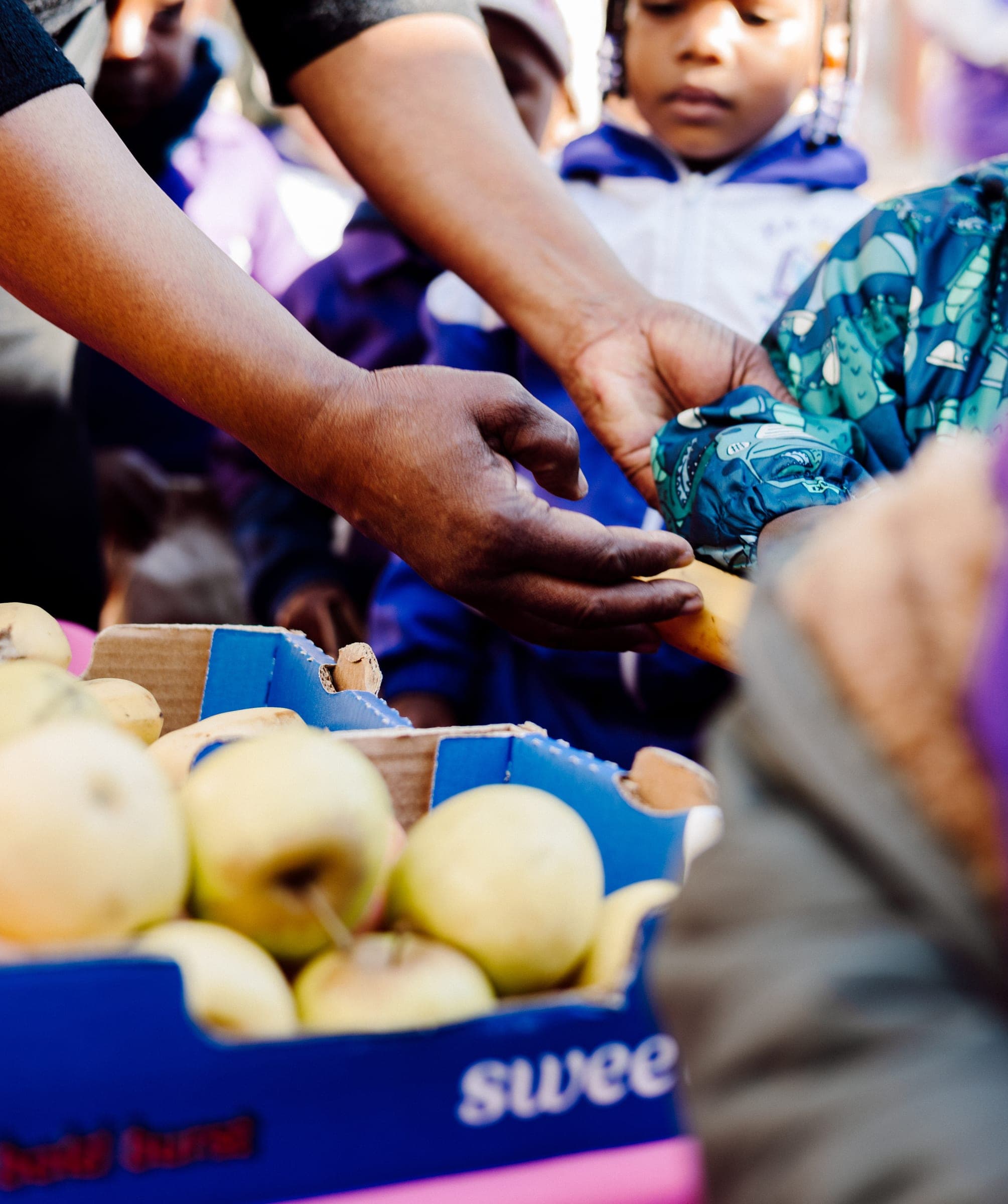 Hands handing fresh fruit to children during the Ba-Tliseng support visit